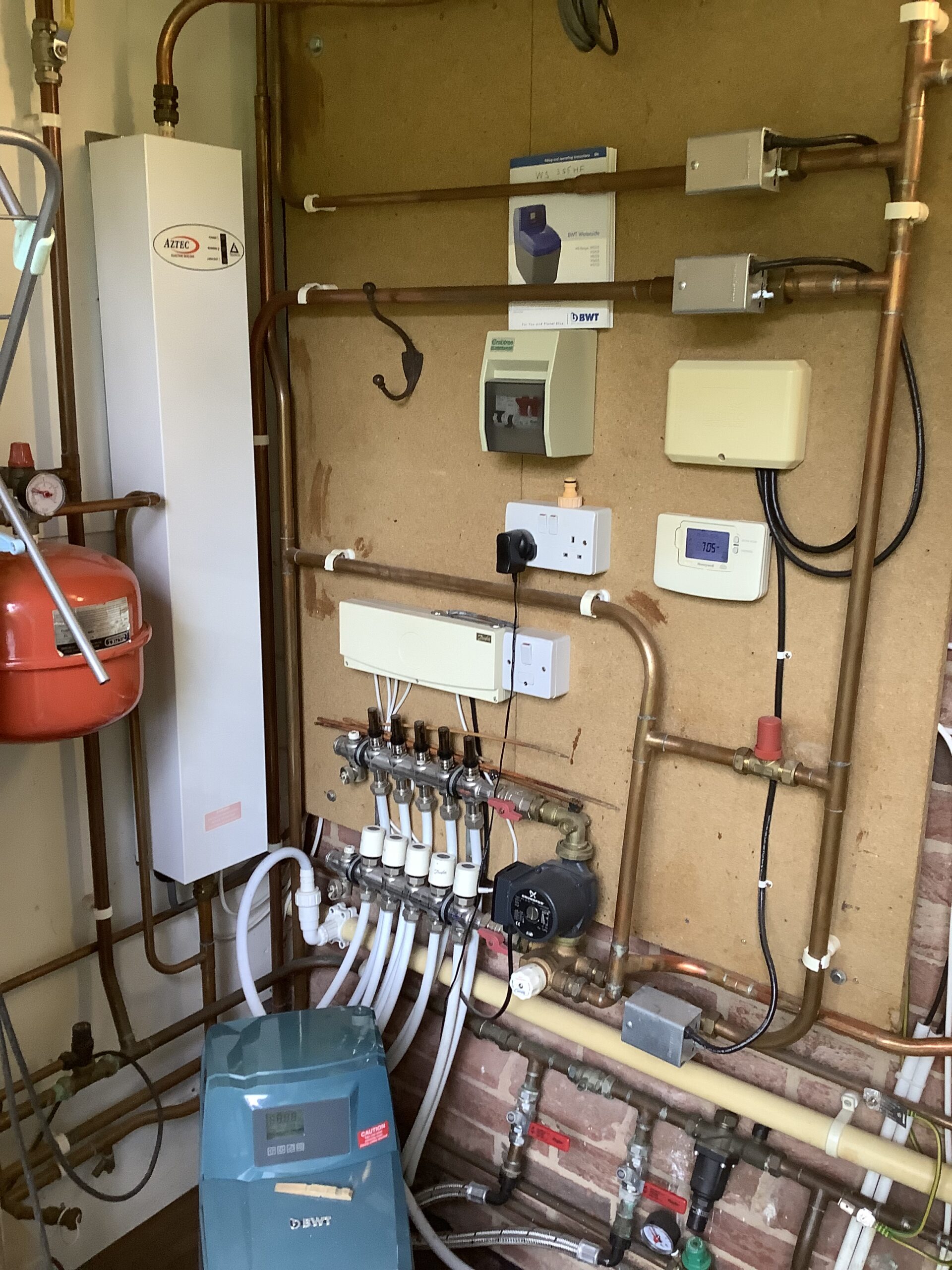 Boiler, copper pipework and underfloor heating manifold in a utility cupboard